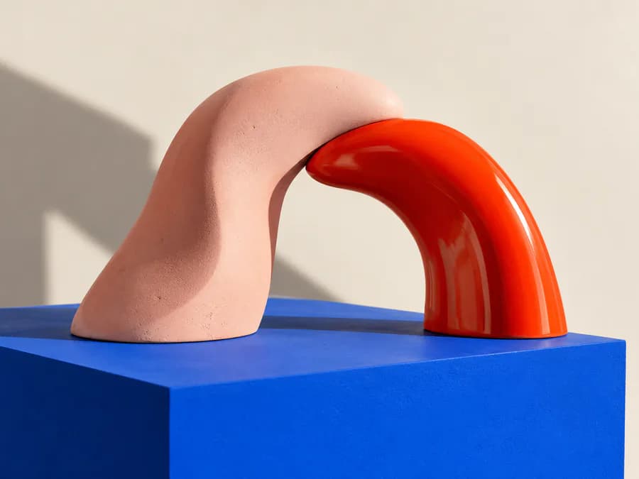 Sculpture en arche rose et rouge posée sur un socle bleu